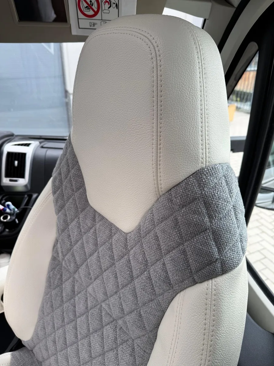 Detail van grijze geweven bekleding en een crèmekleurige hoofdsteun